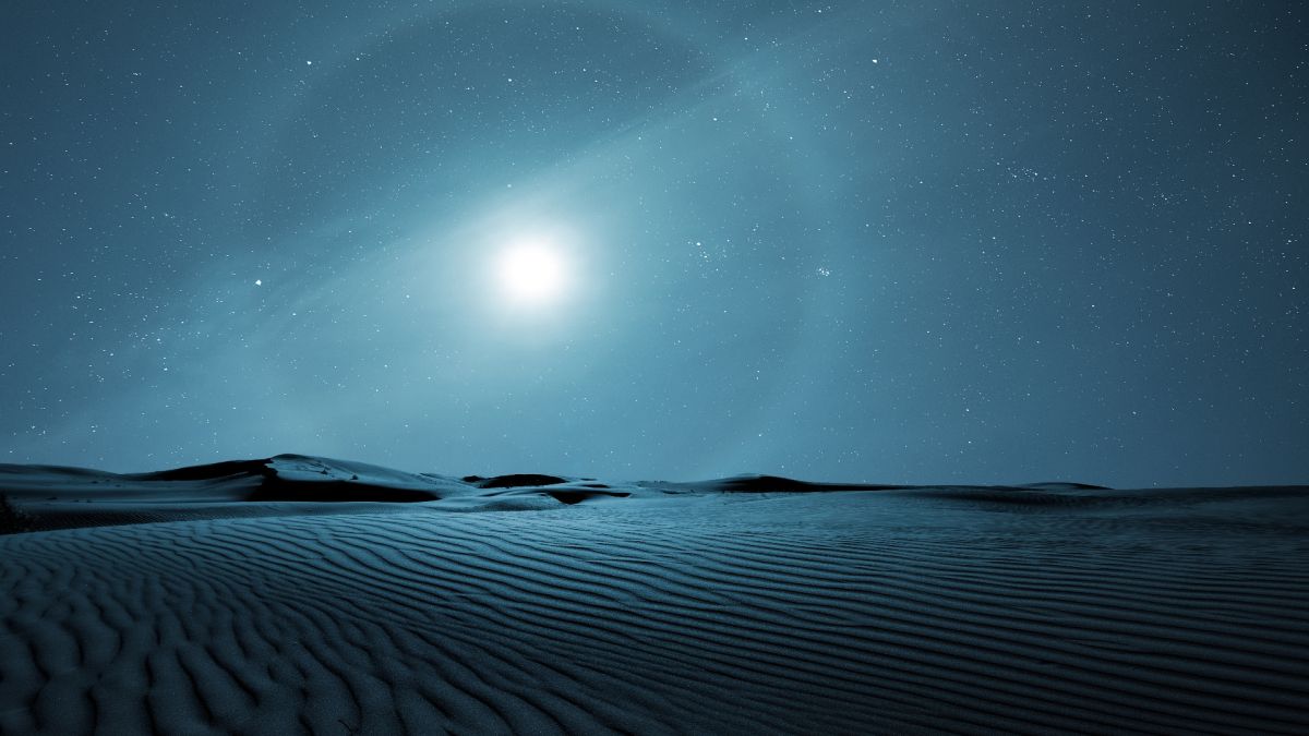 moon halo in the sky above sweeping desert sand dunes.
