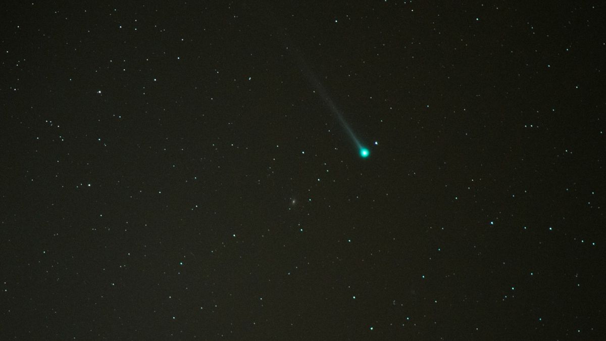 A greenish comet streaks through the night sky.