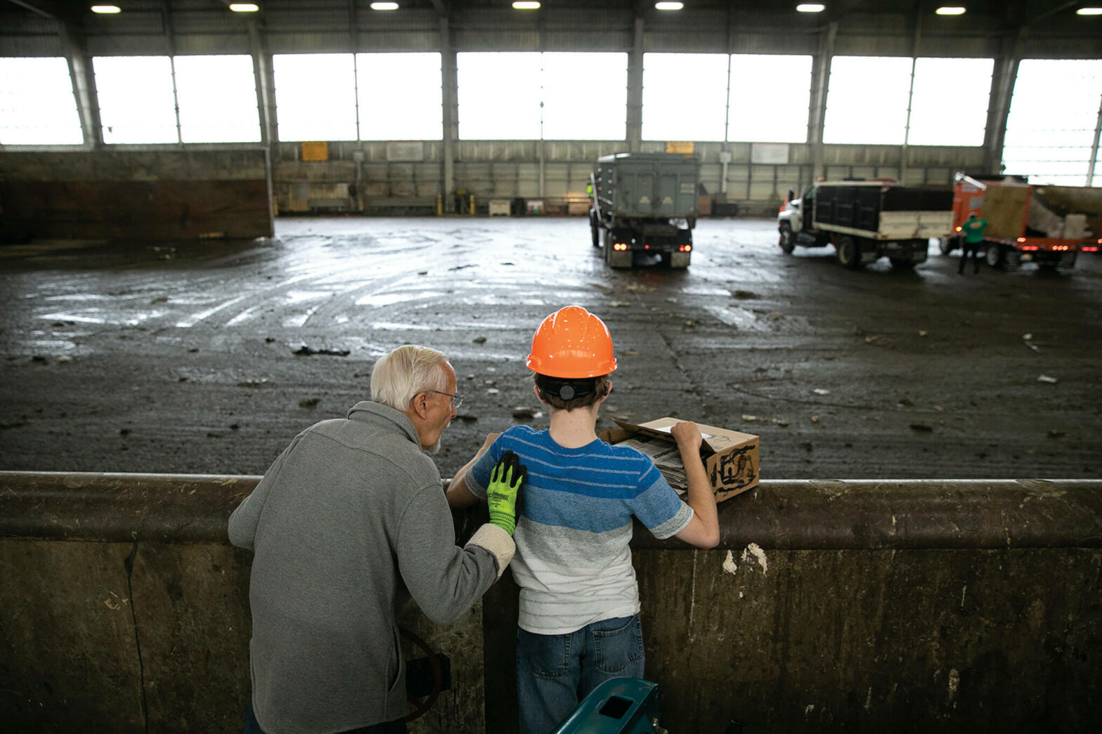Joel Christensen, 24, cannot see or fully hear due to infantile refsum disease. With grandfather Harold at his side, Christensen tosses trash into the pit at the Airport Road Transfer Station in Everett. Going to the transfer station is one of Christenens favorite activities. The vibration of humming machinery, the whooshing of front end loaders and the tactile nature of his familys trash all stimulate his strongest senses. (Photo by Ryan Berry)