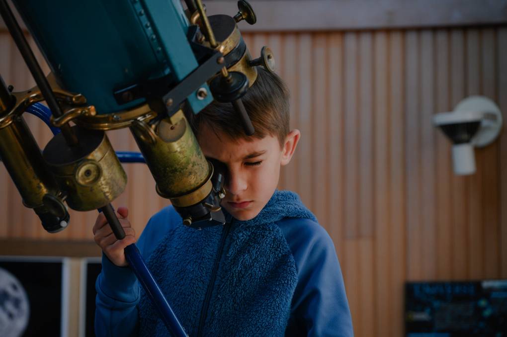 A kid is looking through a telescope.